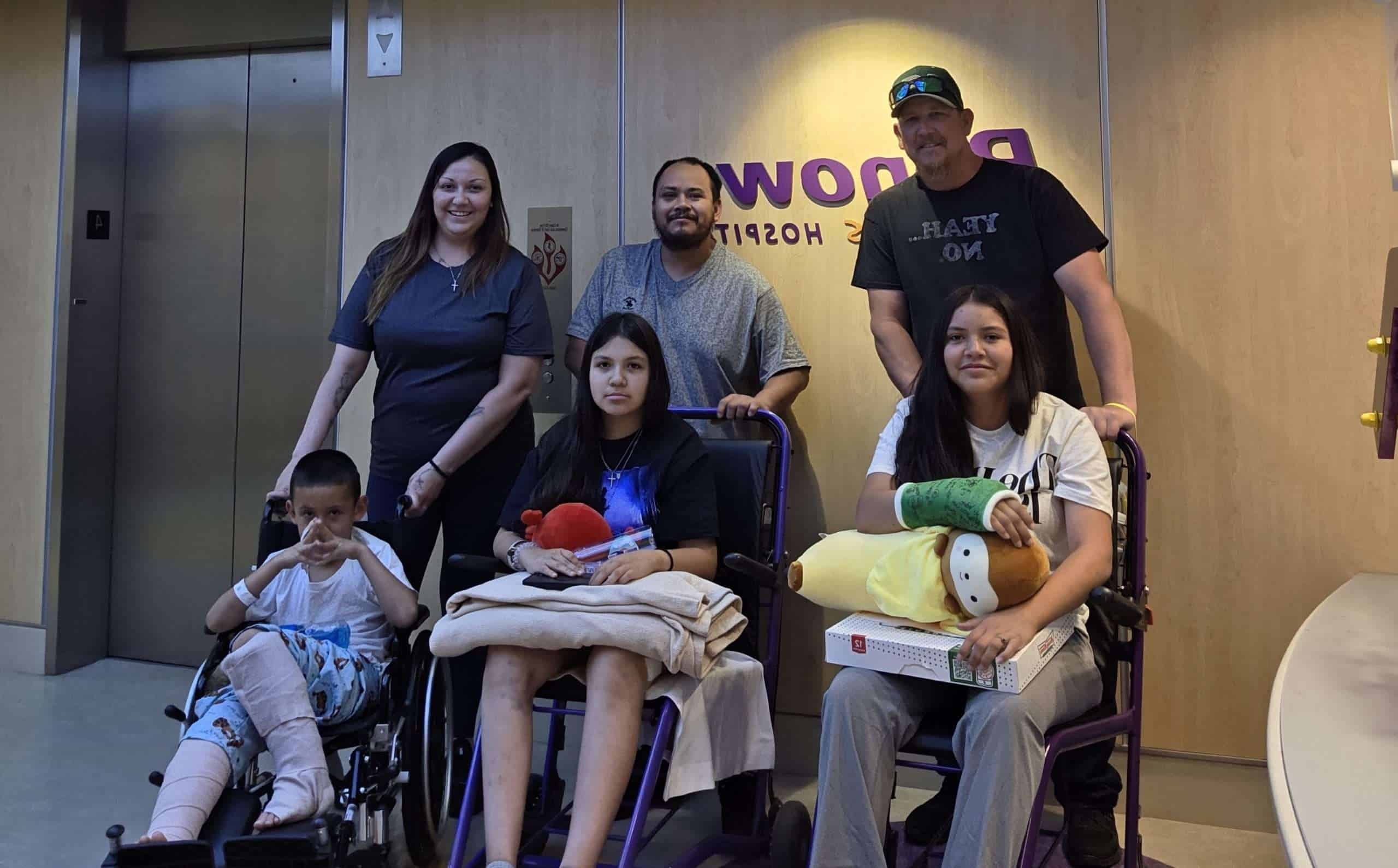 Three adults behind three wheelchairs, all holding kids.